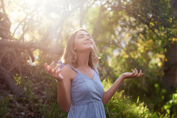 Беззаботная женщина с руками, наслаждающаяся солнечным светом в лесу
