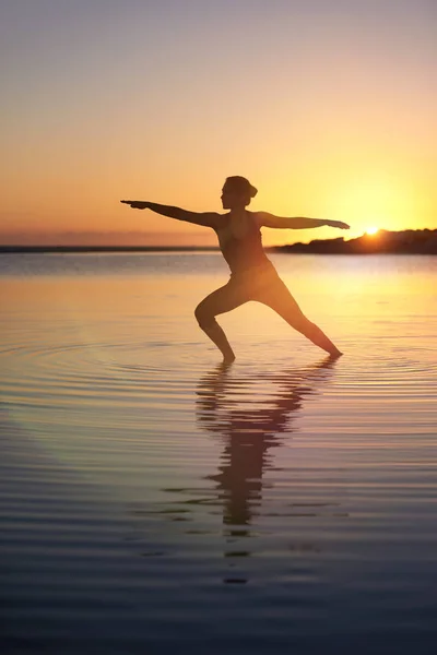 海上日落 海水附近的浅水 女性练习瑜伽 图库图片