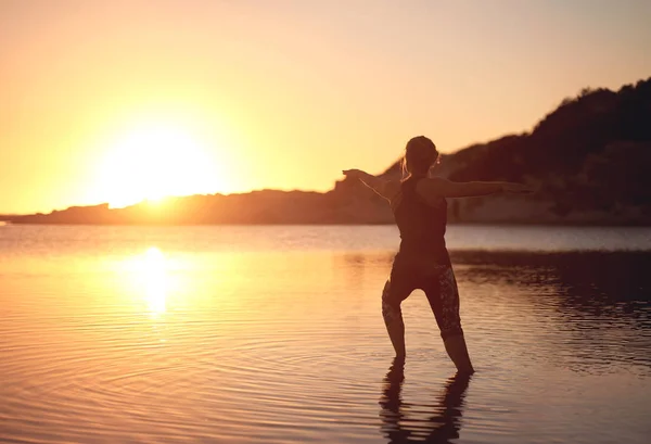 Frau Macht Yoga Flachen Wasser Strand Bei Sonnenuntergang lizenzfreie Stockbilder