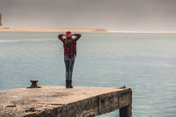 Woman standing on pier with raised arms feeling freedom