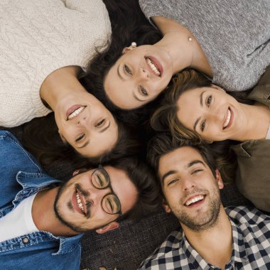 Yerde uzanmış kameraya bakan bir grup arkadaşın üst görüntüsü