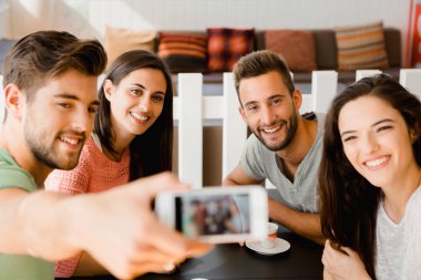 Kahve dükkanındaki bir grup arkadaş birlikte selfie çekiyorlar. 