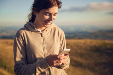 Smartphone kullanarak ve tepe üzerinde yürürken kısa mesaj gönderme kadın 