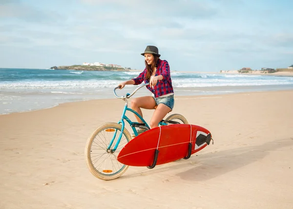 サーフボードでビーチで彼女の自転車に乗って美しいサーファーの女の子 — ストック写真