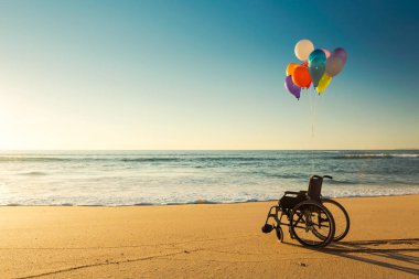 Wellchair on a beach with colored  ballons  clipart