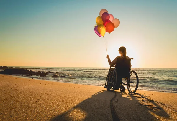 ビーチでカラフルな風船を持つ車椅子の障害者の女性 — ストック写真
