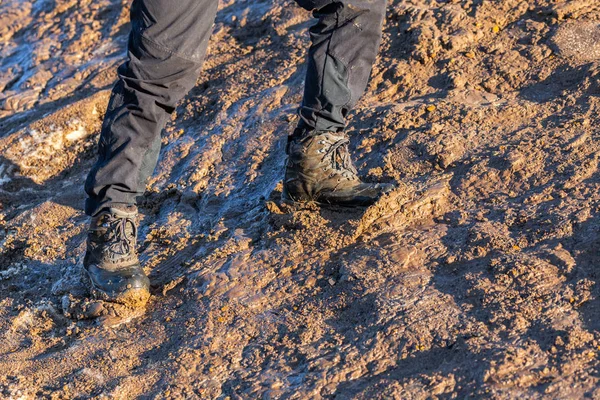 legs in gray pants and trek boots hiking upwards on muddy hill at evening sunlight