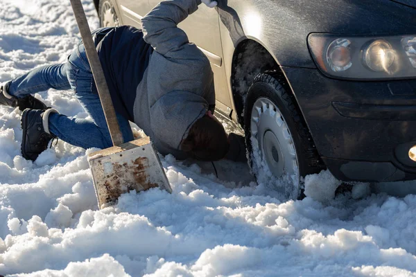 Hombre trabajando en el coche atrapado en la nieve en la rodilla con la pala a la luz del día offroad — Foto de Stock