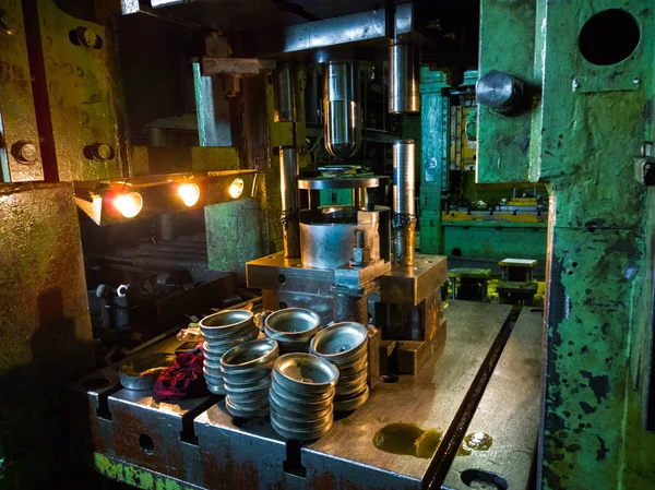 dirty used low tech stamping press producing round aliminium parts in dark environment