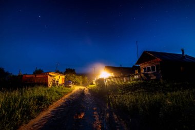 Yaz aylarında köy evi üzerinde yıldızlı gece gökyüzü. Giriş üzerinde bir ampul Lamba ile ahşap ev. Rusya.