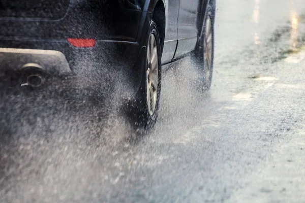 rain water splash flow from wheels of black car moving fast in daylight city with selective focus