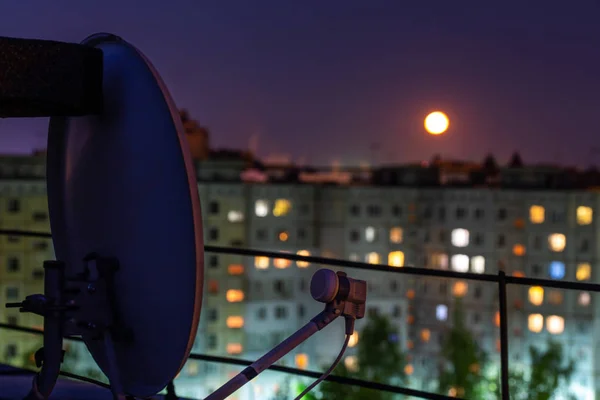 satellite dish on russian condominium roof at full moon night with selective focus and blur