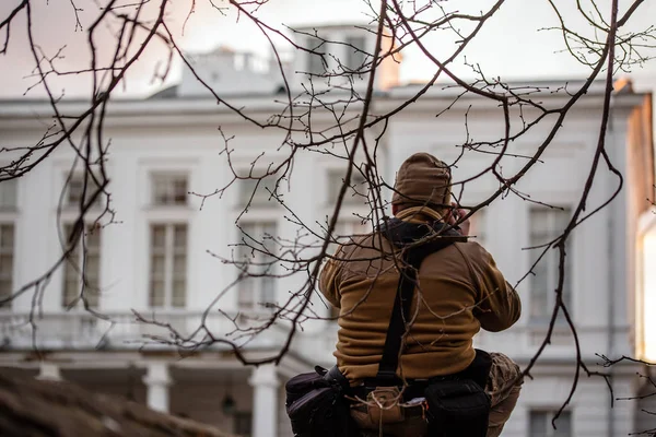 Sneaky professional photographer shooting private white building facade from fence under tiny brcnches.