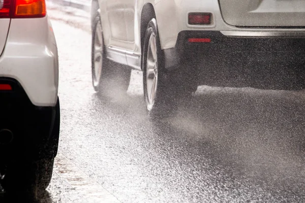 Regenwater splash flow van wielen van witte auto's die snel bewegen in daglicht stad met selectieve focus — Stockfoto