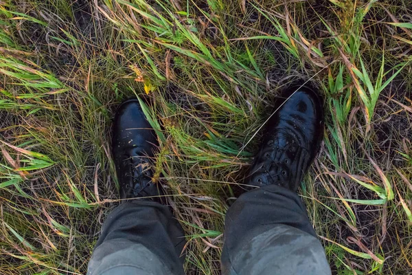 Feet in wet black army boots and green cotton pants in autumn grass gonzo downward point of view.