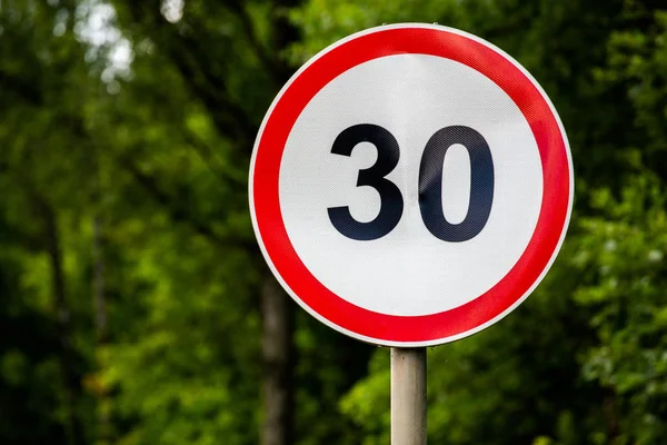 Road sign speed limit 30 kilometers per hour on green forest background with selective focus