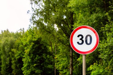 Road sign speed limit 30 kilometers per hour on green forest background with selective focus clipart
