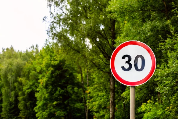 Limit prędkości znak drogowy 30 kilometrów na godzinę na tle zielonego lasu z selektywnej ostrości — Zdjęcie stockowe
