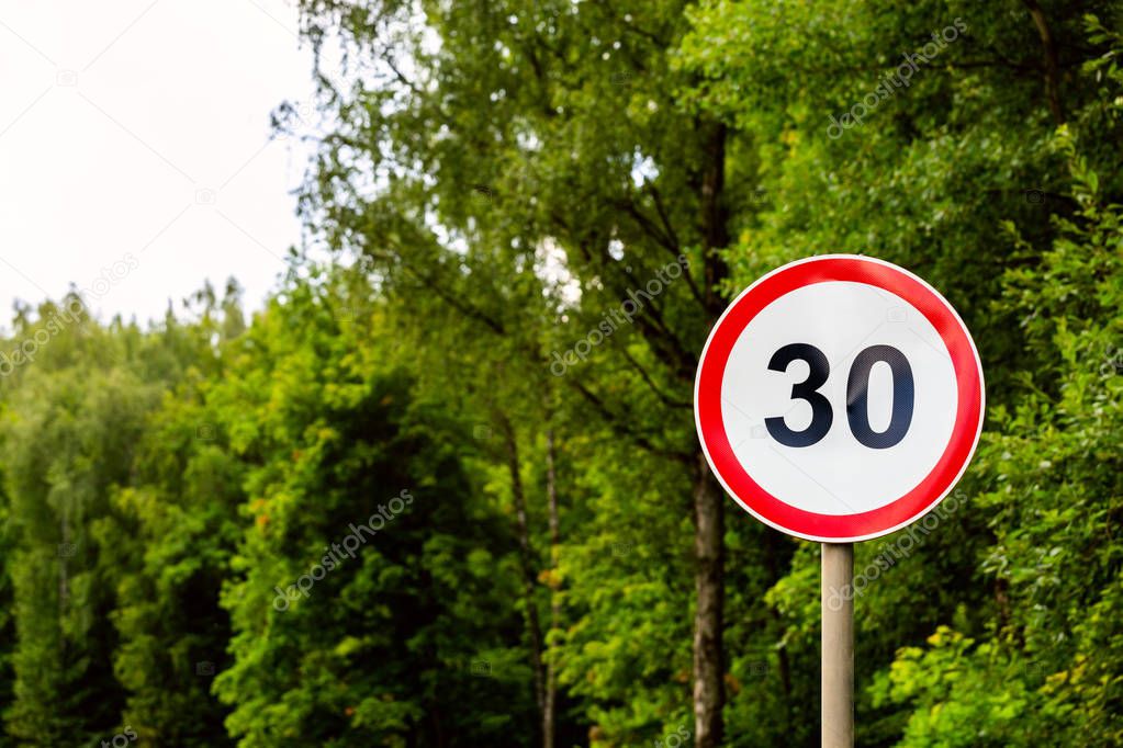 Road sign speed limit 30 kilometers per hour on green forest background with selective focus