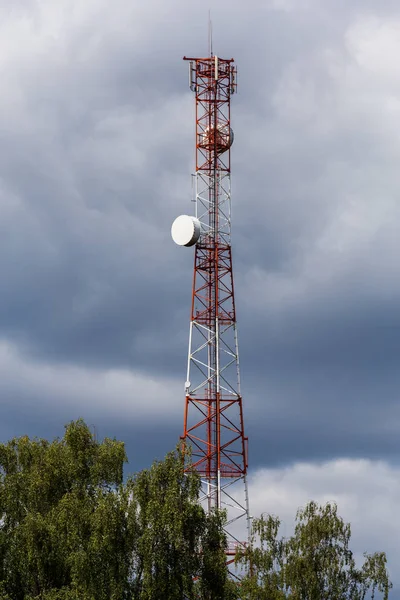 Rot-weißer Telekommunikationsturm mit Spitze eines grünen Baumes am blauen Himmel mit Wolkenhintergrund — Stockfoto