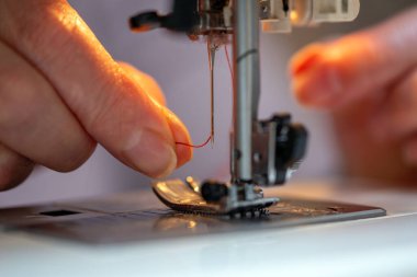 Büyükanne parmakları dikiş makinesine kırmızı bir iplik sokuyor. İğne, yakın plan.