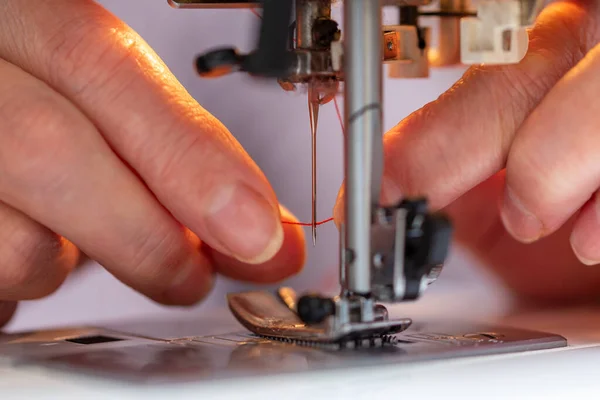 Dedos de mujer mayor insertando un hilo rojo en una aguja de máquinas de coser, primer plano — Foto de Stock