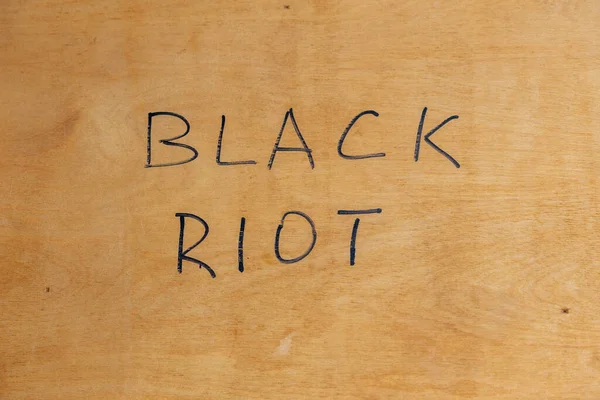 Le parole riot nero scritto a mano con pennarello nero sulla superficie del compensato piatto. Concetto . — Foto Stock