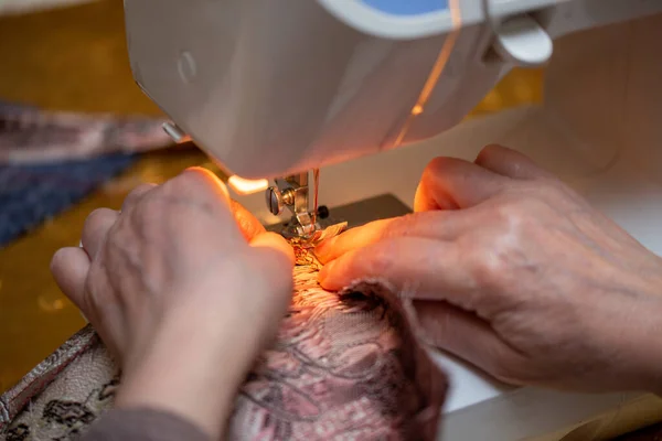 Una vista de cerca del proceso de costura, mano de la anciana utilizando la máquina de coser, técnica de enfoque selectivo — Foto de Stock