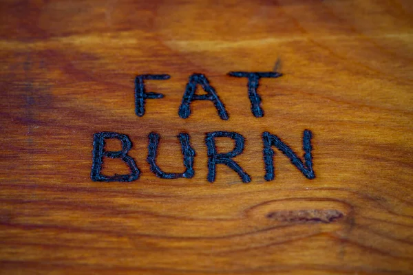 Słowa spalanie tłuszczu handritten na drewnianej powierzchni z palnikiem drewna — Zdjęcie stockowe