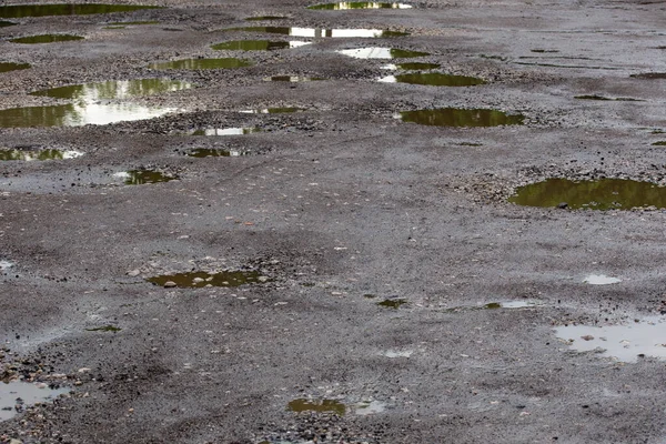 Asfalto estrada danificado acidentado com múltiplas poças após a chuva durante o dia de verão — Fotografia de Stock