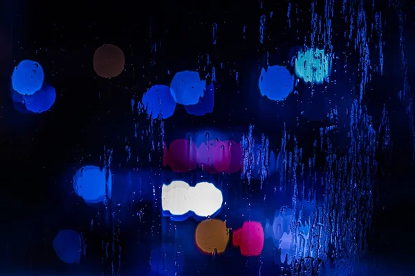 Um fundo abstrato de luzes da polícia vermelho e azul bokeh através de vidro molhado à noite close-up com foco seletivo — Fotografia de Stock