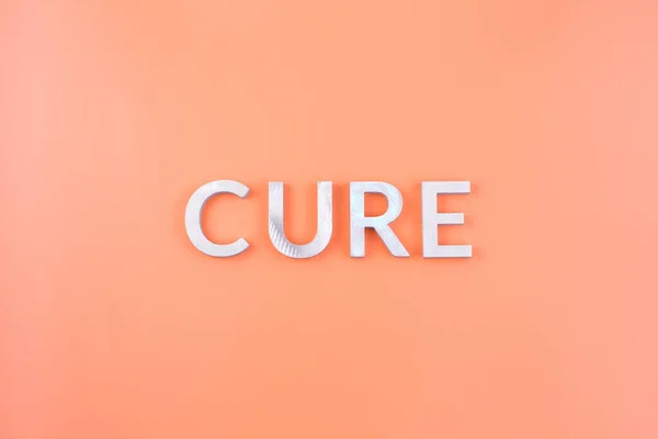 Kata cure diletakkan dengan huruf aluminium tebal pada warna pastel oranye muda — Stok Foto
