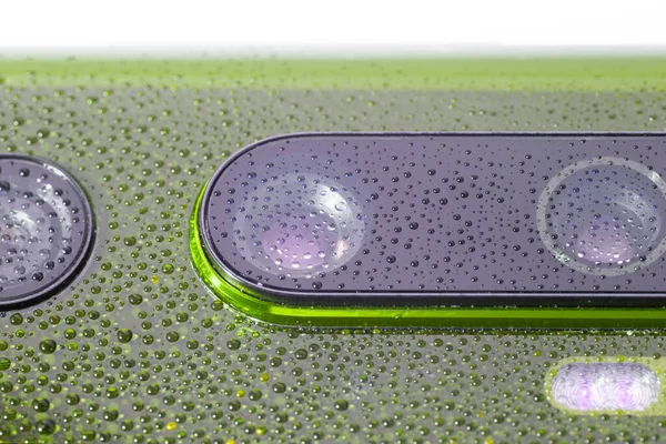 Lente de la cámara del teléfono verde cubierta con pequeñas gotas de agua - primer plano con enfoque selectivo y desenfoque — Foto de Stock