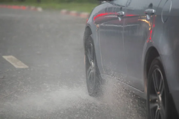 Regen water spatten stroom van wielen van zilveren auto snel in daglicht stad met selectieve focus. — Stockfoto