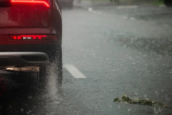 Regen water spatten stroom van wielen van rode auto snel in daglicht stad met selectieve focus. — Stockfoto