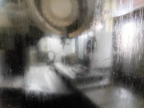 wet and dirty glass of cnc milling machine - close-up with selective focus and blur