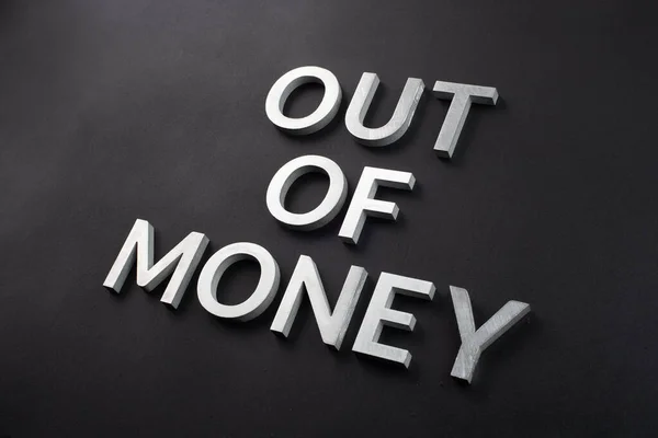 the words out of money laid with white brushed metal letters on flat black surface with diagonal composition and selective focus