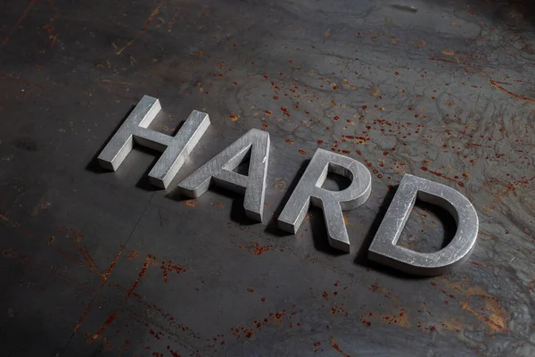 La parola hard laid con lettere in metallo argento su sfondo superficie piana in ferro bruciato arrugginito — Foto Stock