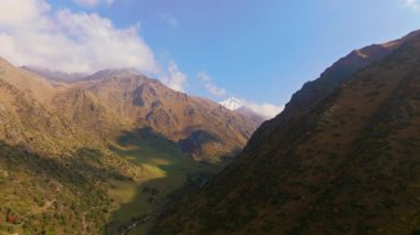 Kırgızistan 'da güneşli bir günde bulutlu ve karla kaplı sonbahar dağlarının hava manzarası.