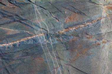 Close-up view of a dark gray metamorphic rock exhibiting distinct light-colored mineral veins that cut across the darker foliation, along with several intersecting fractures, under natural daylight.