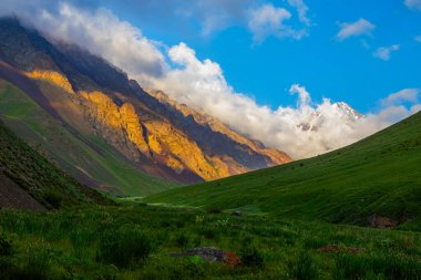Serene mountain range illuminated by sunset light. Lush vegetation and deep valleys create a peaceful and dramatic atmosphere in this breathtaking natural landscape. in Kyrgyzstan