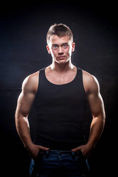 在黑暗背景下身穿黑色运动衫的年轻肌肉男 — 图库照片