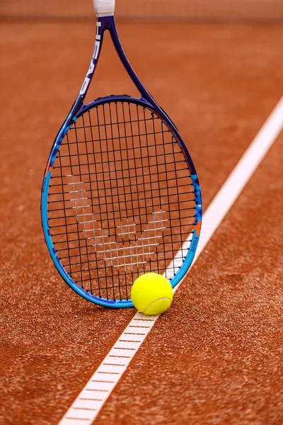 Racket with a tennis ball on a red clay court.