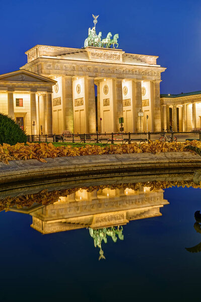 The famous Brandenburg Gate in Berlin at night, reflected in a fountain