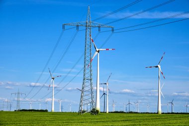 Overhead power lines and wind engines on a sunny day seen in Germany clipart
