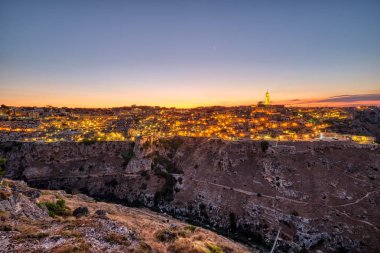 Matera 'nın güzel eski kasabası ve gün batımından sonra Gravina nehrinin kanyonu manzarası.