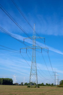 Arkasında rüzgar türbinleri olan elektrik direği ve elektrik hatları.