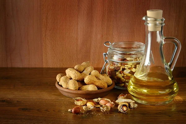 Peanut oil in bottle and dry nuts on wooden table. Copy space