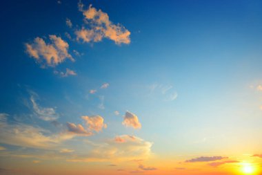 Parlak mavi gökyüzüne ve turuncu bulutlara karşı güneş ışığıyla manzaralı bir gün batımı.