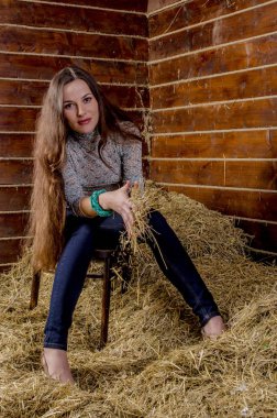 Uzun kahverengi saçlı ve samanlı bir ahırda kot pantolon giyen bir kız.